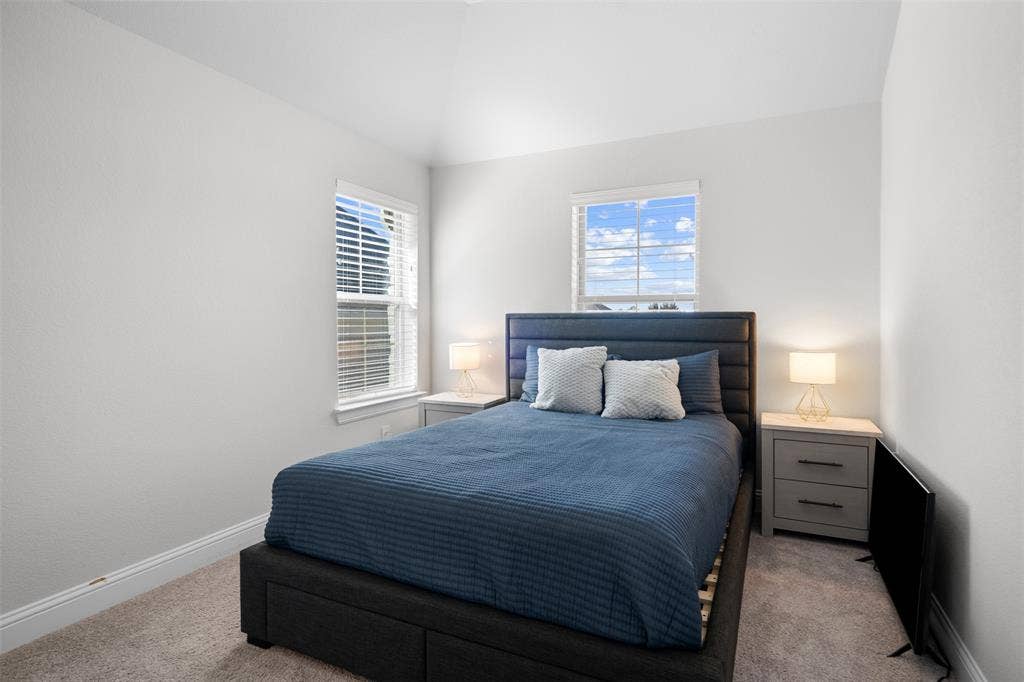 Vaulted ceiling, two windows with blinds, light gray walls, and carpet flooring