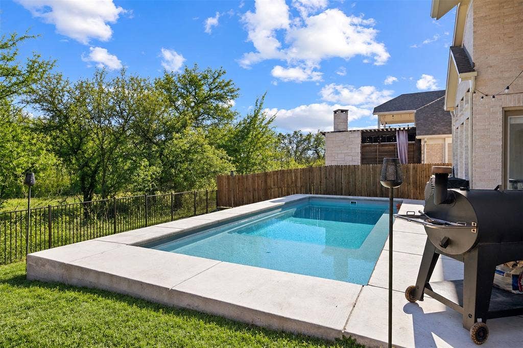 Backyard featuring a rectangular swimming pool with a concrete surround, a wood fence, and a black metal fence