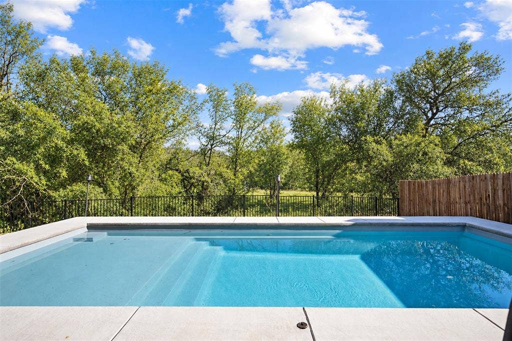 In-ground swimming pool with integrated steps, concrete surround, black metal fencing, and a section of wood privacy fencing