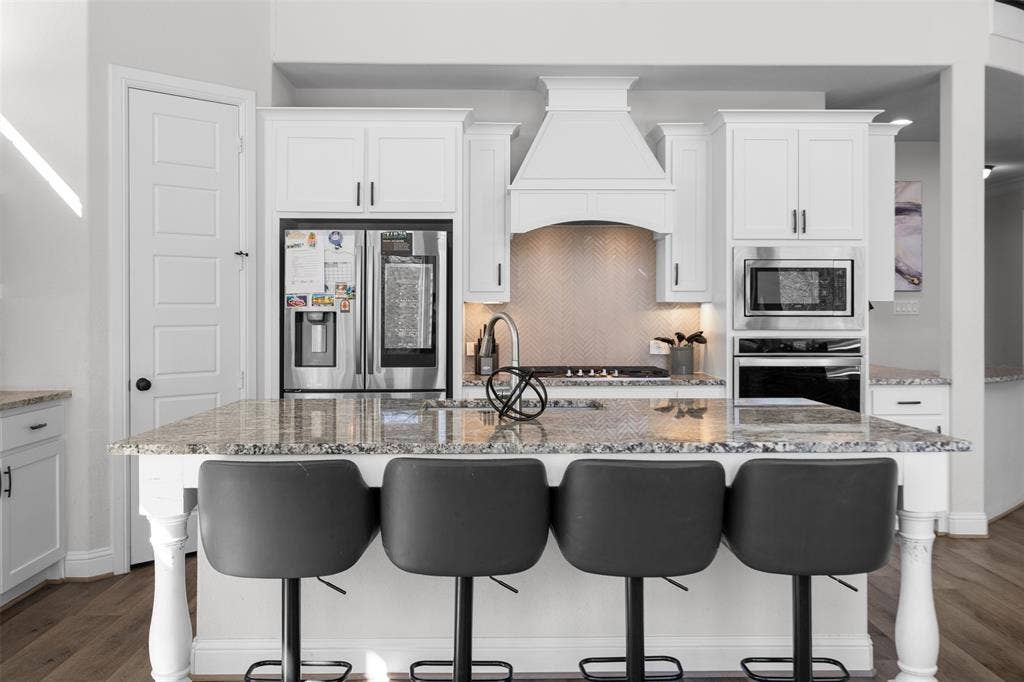 Kitchen island with granite countertop, white cabinetry, stainless steel appliances, and wood-finish flooring