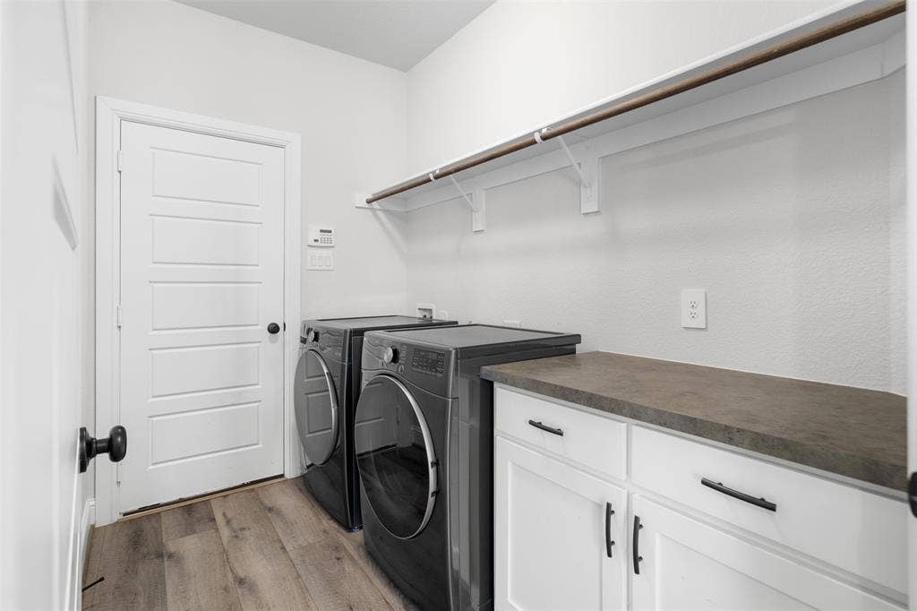 Laundry area featuring wood-finish flooring, white cabinetry with black hardware, a grey countertop, and an overhead clothes rod