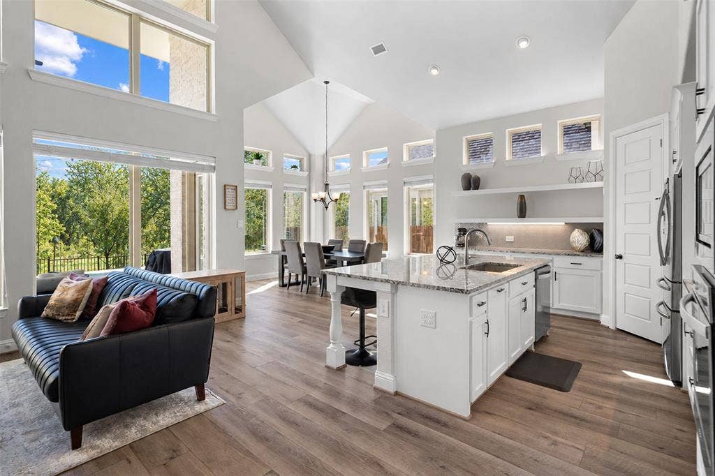 Wood-finish flooring throughout, vaulted ceiling, recessed lighting, white cabinetry, and a kitchen island with a granite countertop