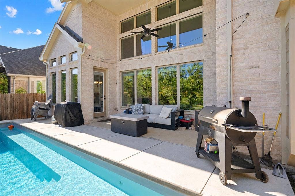 Outdoor living space featuring a swimming pool, expansive patio, brick exterior, and large windows