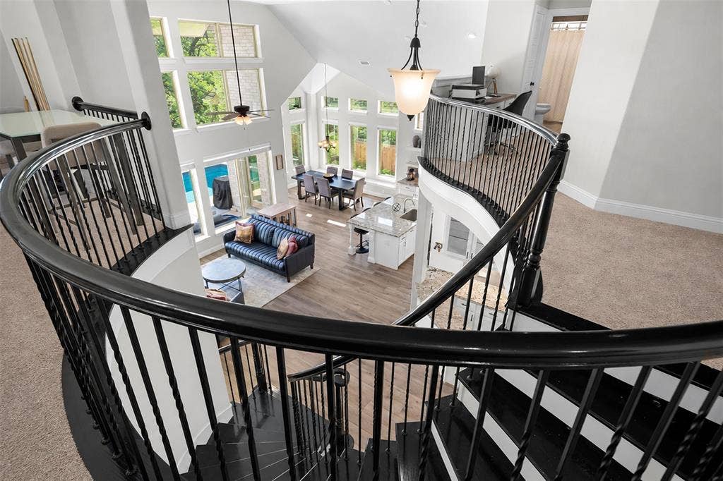 Curved staircase with black railings, vaulted ceiling, extensive window array, wood-finish flooring, and a kitchen island with seating