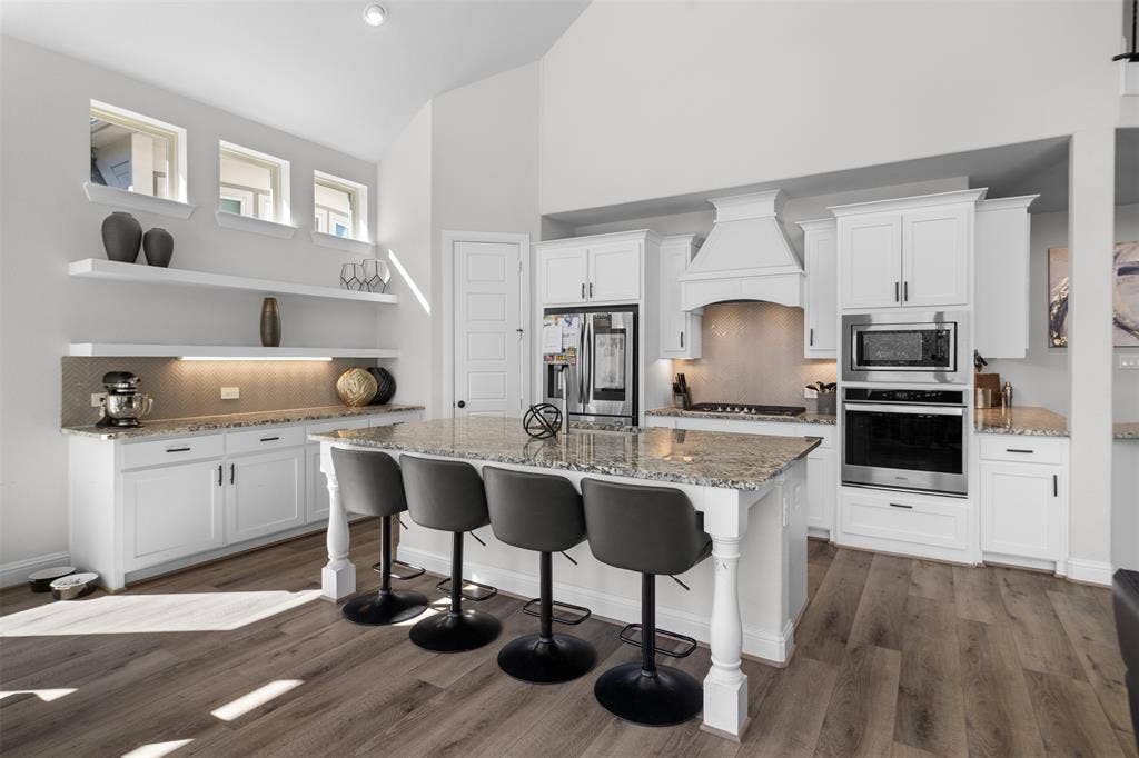 Kitchen featuring white cabinetry, wood-finish flooring, a center island with a stone countertop, stainless steel appliances, and a tiled backsplash