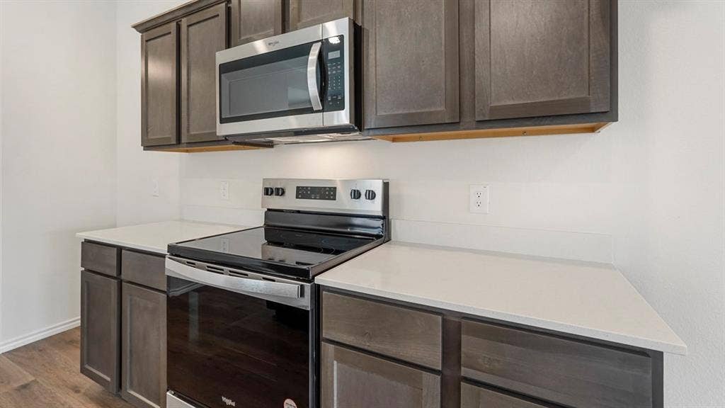 Modern kitchen featuring dark wood-finish cabinetry, light countertops, and a stainless steel range with an overhead microwave