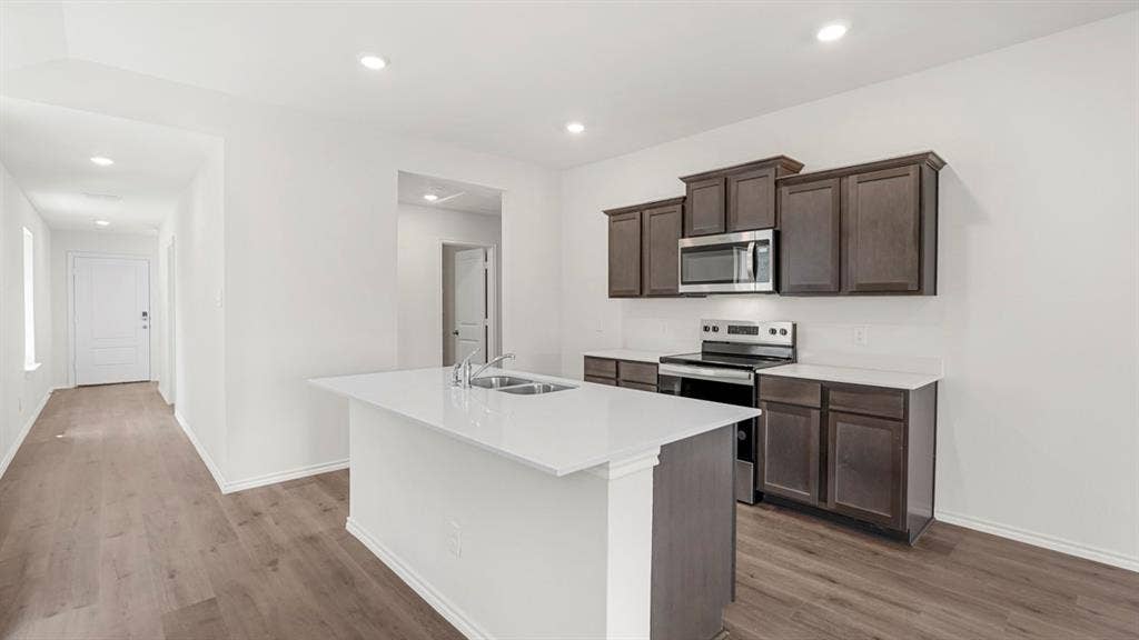 Open-concept kitchen featuring a center island with double sink, dark wood-finish cabinetry, stainless steel microwave, black electric range, and wood-finish flooring