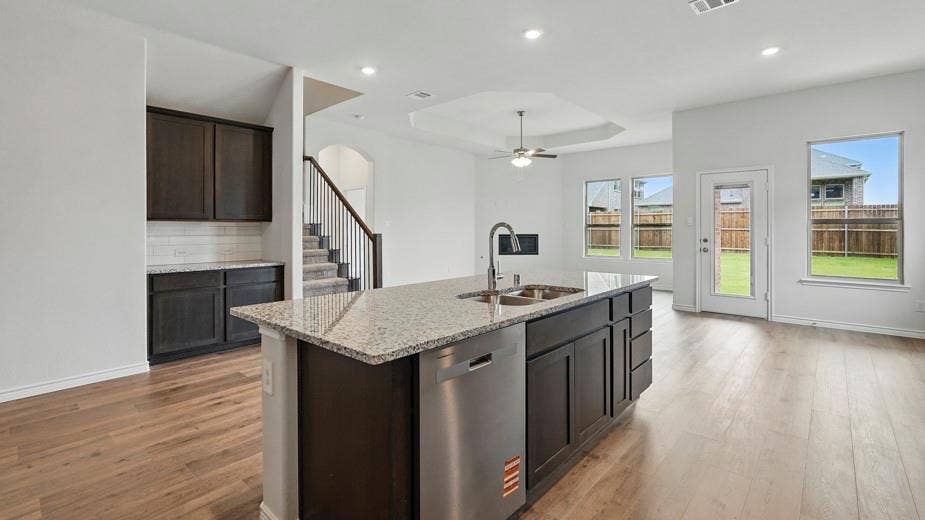 2510 Wesley Avenue, Royse City, TX 75189 Spacious open-concept living area featuring wood-finish flooring, a kitchen island with stone countertop and integrated sink, stainless steel appliances, and abundant natural light from multiple windows and a glass-paneled door