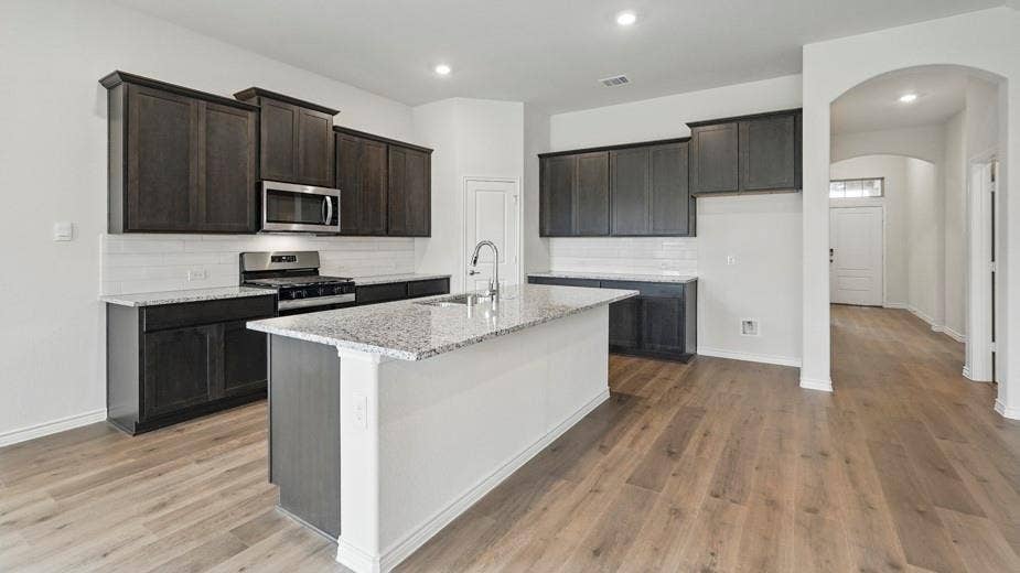 2510 Wesley Avenue, Royse City, TX 75189 Kitchen featuring a central island with a sink, stainless steel appliances, dark wood cabinetry, and light-toned countertops