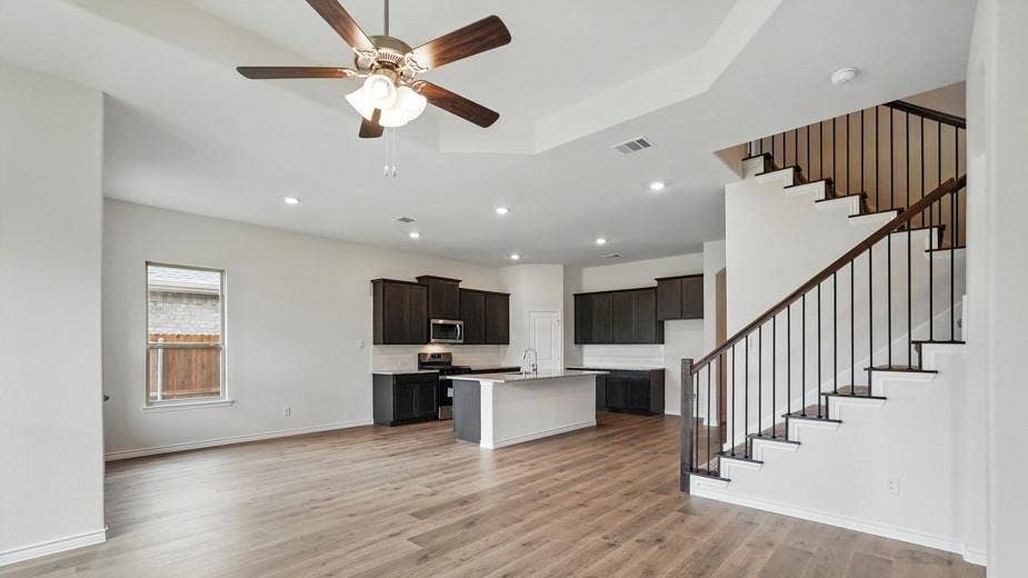 2510 Wesley Avenue, Royse City, TX 75189 Open-concept interior featuring wood-finish flooring, a contemporary kitchen with dark cabinetry and a white island, a staircase with dark wood handrails and black metal balusters, recessed lighting, and a ceiling fan
