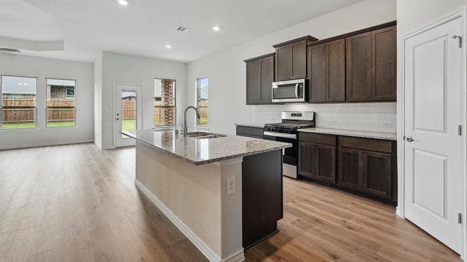 2510 Wesley Avenue, Royse City, TX 75189 Open-concept kitchen featuring an island with a built-in sink, granite countertops, dark wood cabinetry, stainless steel appliances, and wood-finish flooring