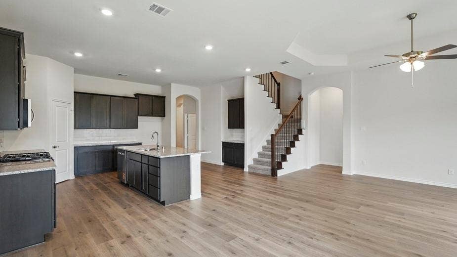 2510 Wesley Avenue, Royse City, TX 75189 Open-concept living space featuring wood-finish flooring, a contemporary kitchen with dark cabinetry and a central island, a multi-level ceiling with a ceiling fan, a carpeted staircase with an iron spindle railing, and recessed lighting