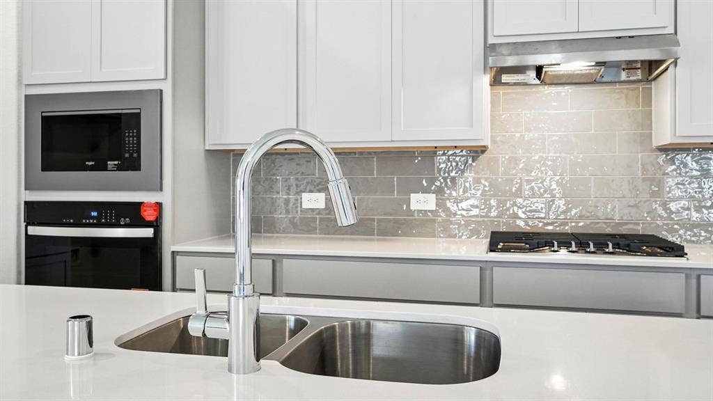 2503 Wesley Avenue, Royse City, TX 75189 Kitchen featuring a dual basin sink with a gooseneck faucet, white shaker cabinetry, light-toned countertops, a built-in microwave, and a gas cooktop with a stainless steel range hood