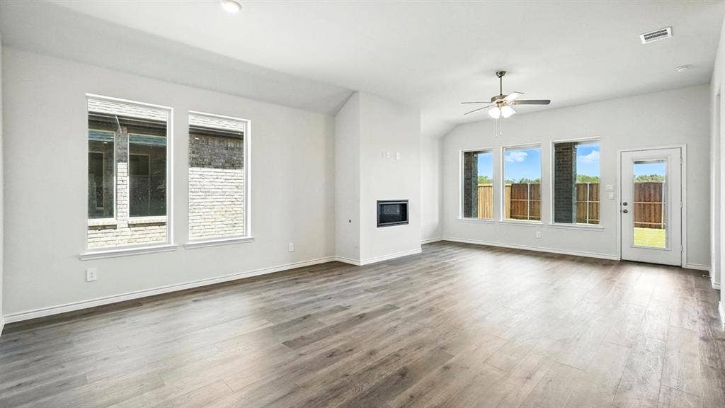 2503 Wesley Avenue, Royse City, TX 75189 Spacious living area featuring wood-finish flooring, a contemporary built-in fireplace, multiple large windows, and a glass-paneled exterior door