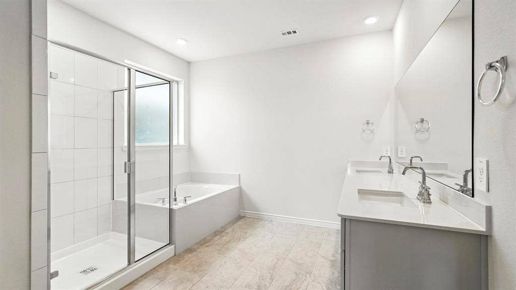 2503 Wesley Avenue, Royse City, TX 75189 Bathroom featuring a glass-enclosed shower, a built-in soaking tub, a double vanity with undermount sinks, a quartz-style countertop, and a large wall-mounted mirror