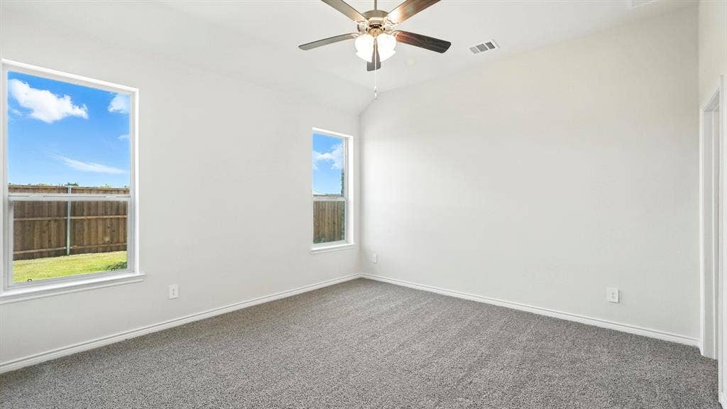 2503 Wesley Avenue, Royse City, TX 75189 Spacious room featuring vaulted ceilings, a ceiling fan with integrated lighting, two double-hung windows, plush gray carpeting, and white baseboards