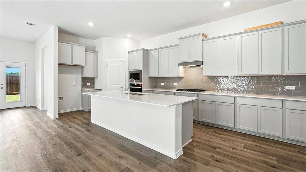 2503 Wesley Avenue, Royse City, TX 75189 Modern kitchen featuring a large central island with a solid surface countertop, light gray cabinetry, and wood-finish flooring