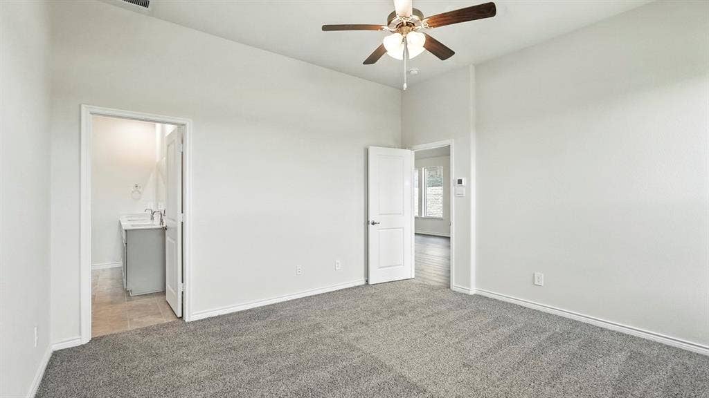 2503 Wesley Avenue, Royse City, TX 75189 Spacious room featuring neutral carpeting, light gray walls, a ceiling fan with integrated lighting, and a white paneled door accessing a bathroom with a modern vanity