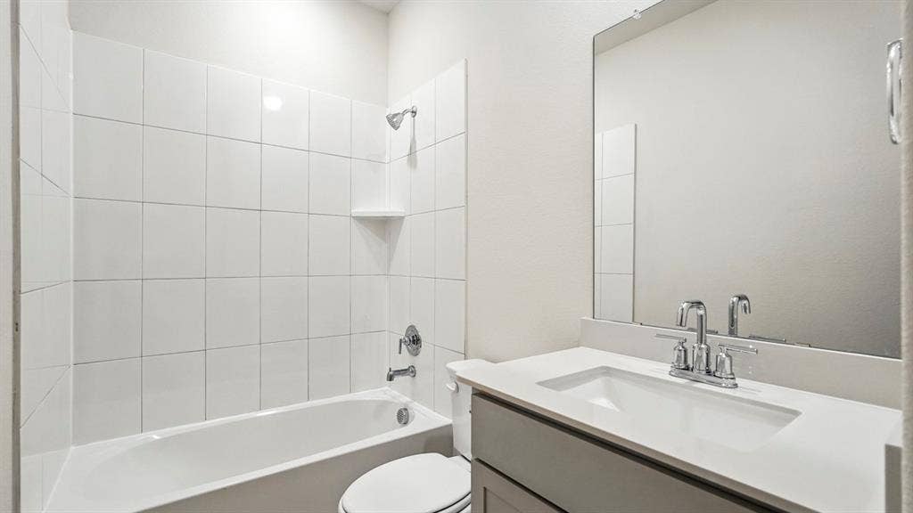 2503 Wesley Avenue, Royse City, TX 75189 Bathroom featuring a white subway tile tub surround, chrome fixtures, built-in shelving, a vanity with an integrated sink, and a framed mirror