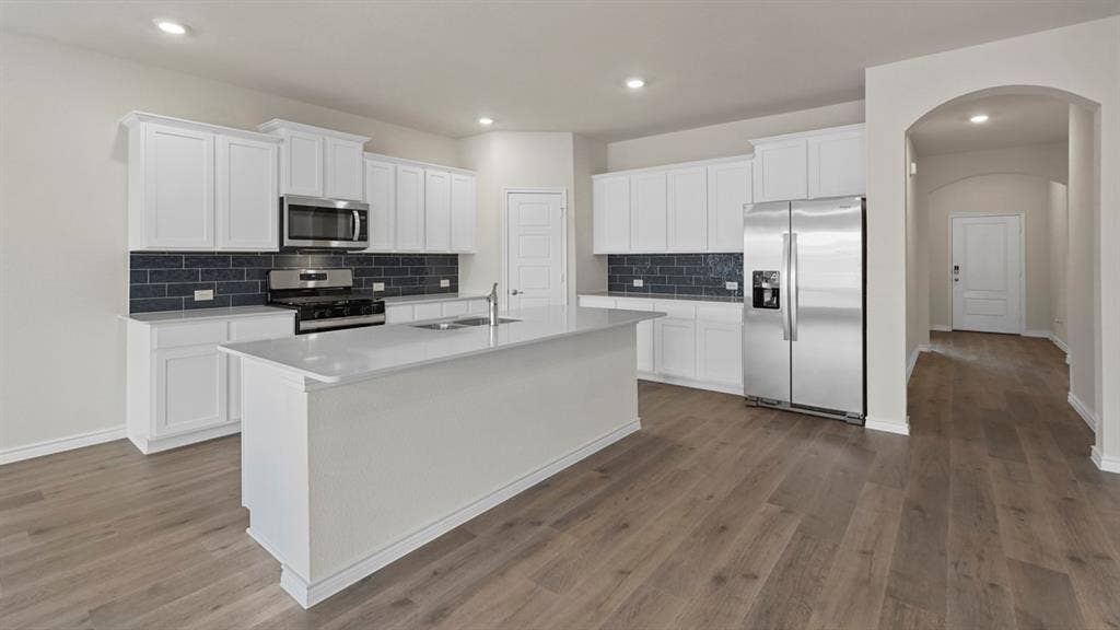 750 Hart Leaf Lane, Lavon, TX 75166 Modern kitchen featuring a central island with an undermount sink, white cabinetry, stainless steel appliances, and wood-finish flooring