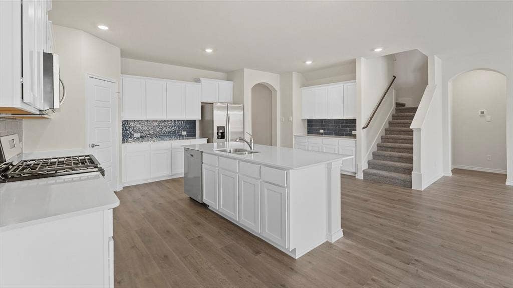 750 Hart Leaf Lane, Lavon, TX 75166 Open-concept kitchen featuring an island with an integrated sink, stainless steel appliances, white cabinetry, and wood-finish flooring