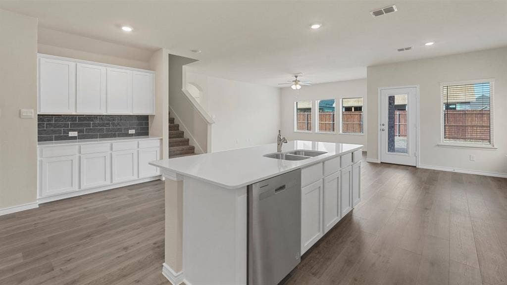 750 Hart Leaf Lane, Lavon, TX 75166 Open-concept living area featuring wood-finish flooring, a kitchen island with dual sinks and dishwasher, white cabinetry with dark subway tile backsplash, and multiple windows for natural light