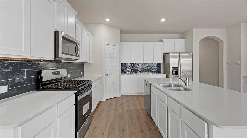 750 Hart Leaf Lane, Lavon, TX 75166 Expansive kitchen featuring white cabinetry, light countertops, wood-finish flooring, stainless steel appliances, and a dark subway tile backsplash