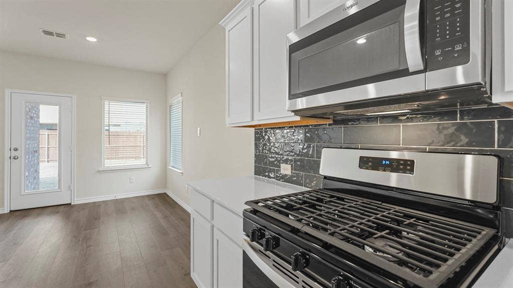 750 Hart Leaf Lane, Lavon, TX 75166 Modern kitchen featuring stainless steel appliances, crisp white cabinetry, a dark subway tile backsplash, light countertops, and wood-finish flooring