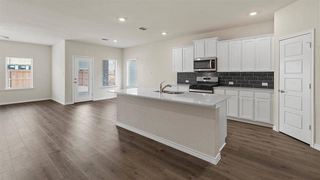 750 Hart Leaf Lane, Lavon, TX 75166 Open-concept living space featuring wood-finish flooring, a kitchen island with an integrated sink, white cabinetry, a stainless steel microwave and range, and a dark subway tile backsplash