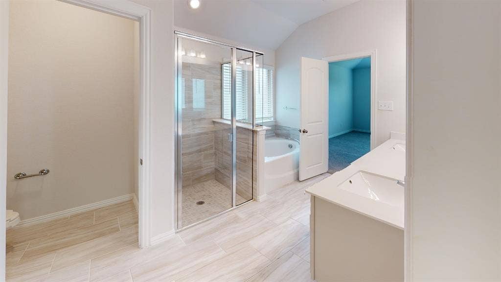 1004 Copper Smith Way, Forney, TX 75126 Spacious bathroom with vaulted ceiling, dual vanity, glass-enclosed shower with tile surround, separate soaking tub, and tile flooring