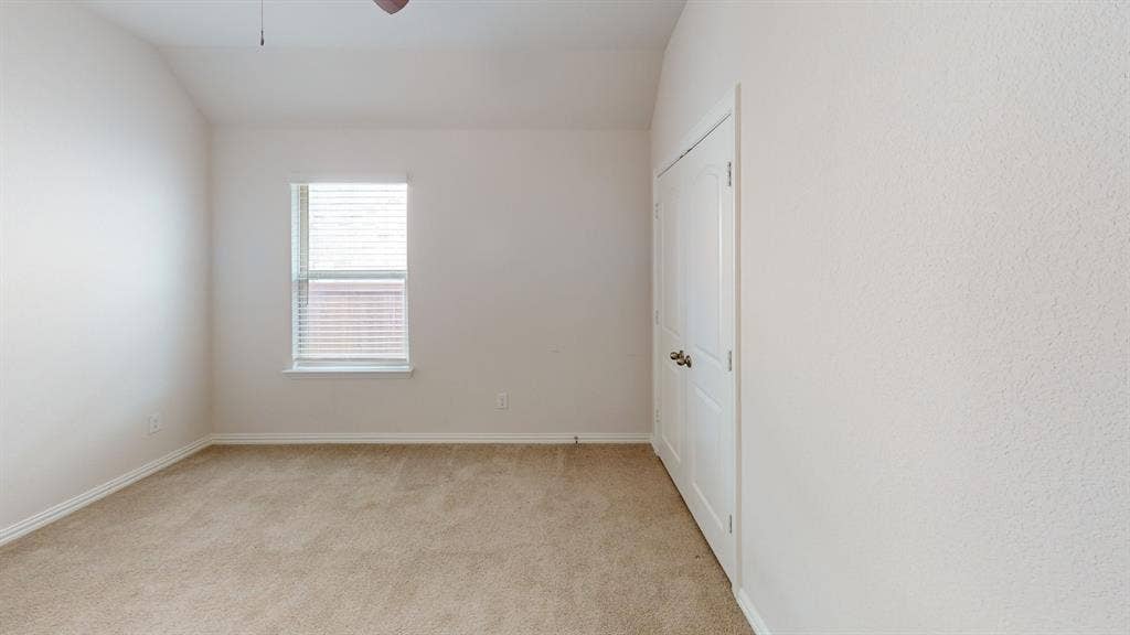 1004 Copper Smith Way, Forney, TX 75126 Carpeted room featuring a single window with blinds, a white door with brass hardware, a ceiling fan, and textured walls