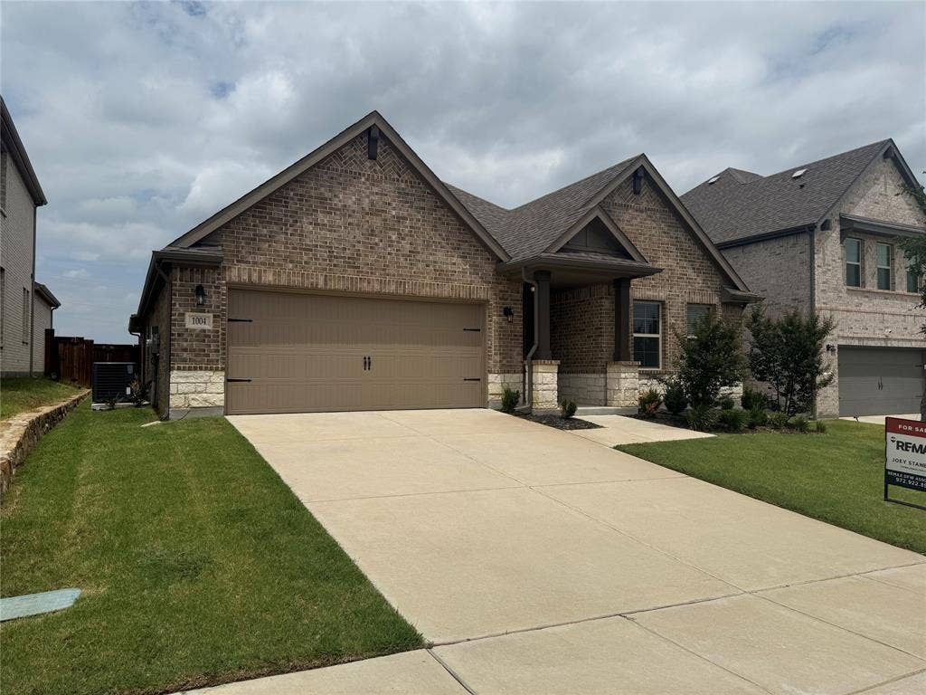 1004 Copper Smith Way, Forney, TX 75126 Brick Colonial home featuring a two-car attached garage, concrete driveway, and manicured front lawn with established landscaping