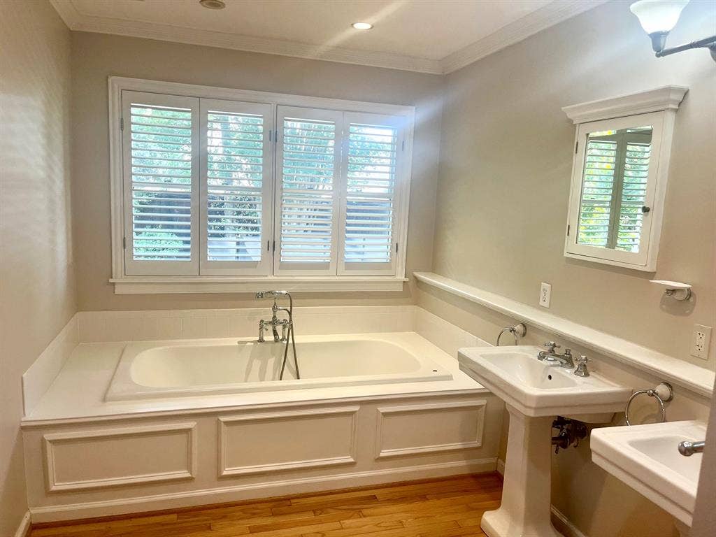 10409 Remington Lane, Dallas, TX 75229 Built-in soaking tub with chrome fixtures, three panel window with plantation shutters, two pedestal sinks, built-in medicine cabinet, and wood-finish flooring