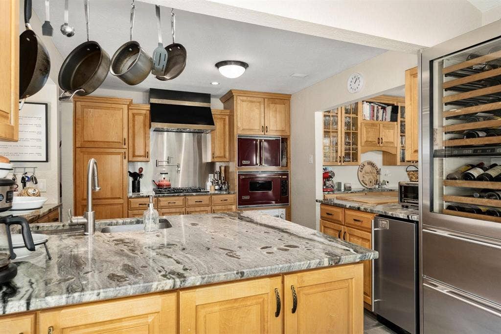 10409 Remington Lane, Dallas, TX 75229 Kitchen featuring wood cabinetry, a large kitchen island with a built-in sink, stainless steel appliances, and a built-in wine refrigerator