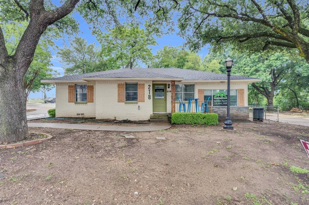 214 W Belt Line Road, #B, Cedar Hill, TX 75104 Brick exterior with a partial stone facade, wood-finish window shutters, a green entry door, and mature trees