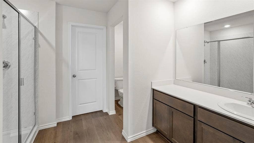809 Brook Lane, Josephine, TX 75135 Wood-finish flooring, glass-enclosed shower, expansive vanity with a single sink, white countertop, and dark wood cabinetry