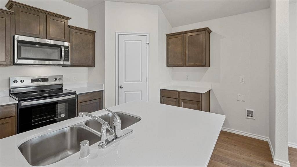 809 Brook Lane, Josephine, TX 75135 Kitchen featuring a stainless steel microwave and range, wood-finish cabinetry, white countertops, and a double basin sink with a chrome faucet
