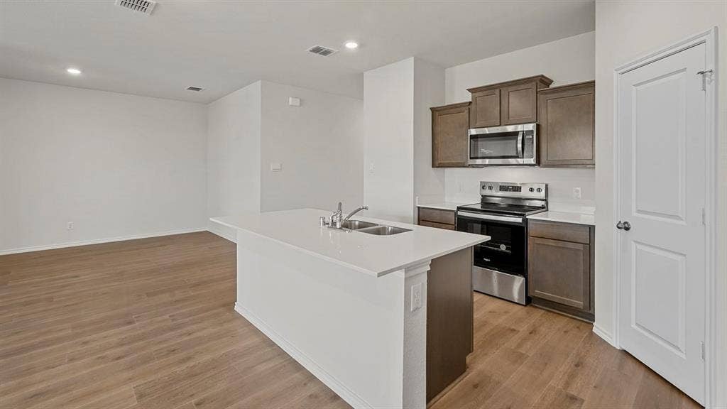 809 Brook Lane, Josephine, TX 75135 Kitchen island with an undermount sink, stainless steel appliances, wood-finish flooring, recessed lighting, and white walls