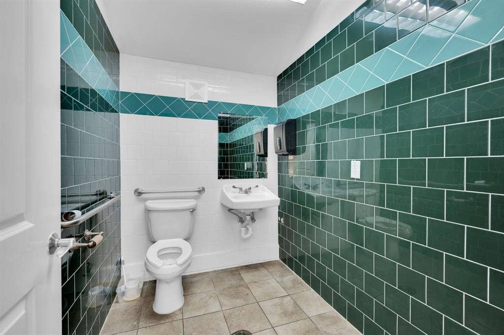 214 W Belt Line Road, #C, Cedar Hill, TX 75104 Ceramic tile wall finishes with decorative accents, ceramic tile flooring, wall-mounted sink, toilet with grab bars, and a wall mirror