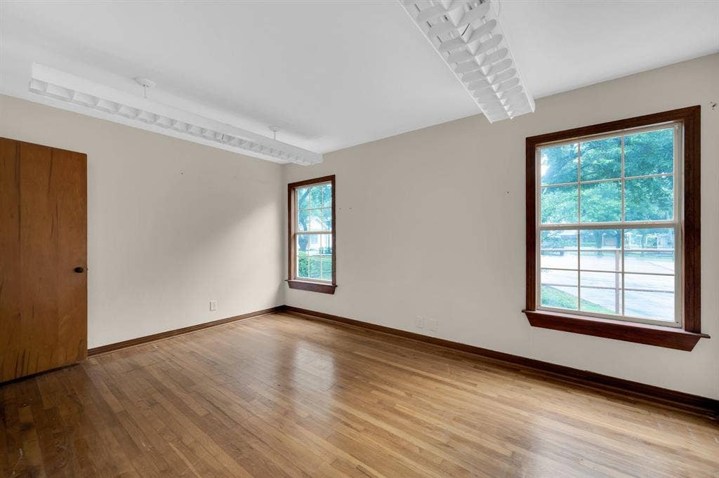 216 W Belt Line Road, Cedar Hill, TX 75104 Hardwood flooring, two large windows with wood trim, ceiling-mounted fluorescent lighting, and a wood-panel door