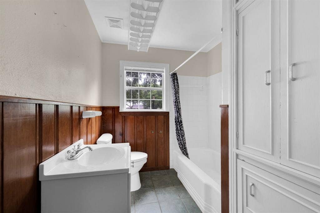 216 W Belt Line Road, Cedar Hill, TX 75104 White vanity with integrated sink, wood-paneled wainscoting, white bathtub, tiled flooring, and built-in white cabinetry