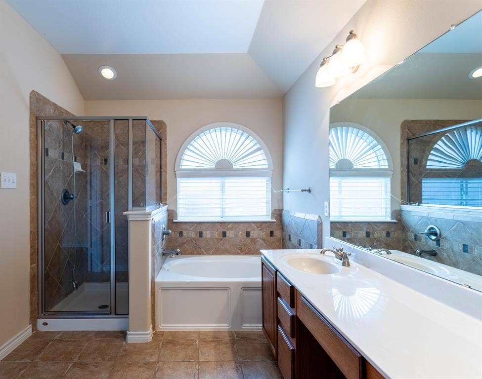 6509 Hickory Hill Drive, Plano, TX 75074 White bathtub with arched window, glass-enclosed shower, wood-finish vanity with white countertop, and tiled flooring