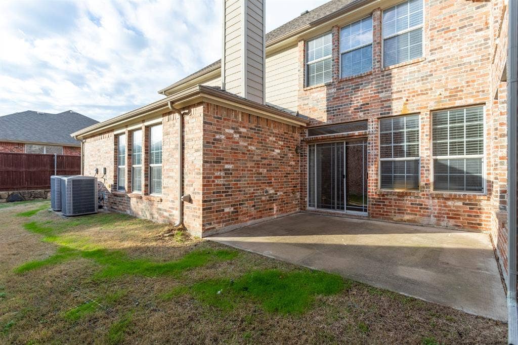 6509 Hickory Hill Drive, Plano, TX 75074 Brick exterior with multiple windows, concrete patio, sliding glass door, and a grassed yard area