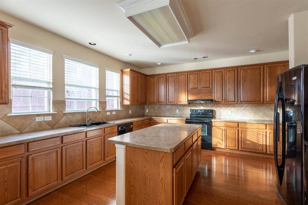 6509 Hickory Hill Drive, Plano, TX 75074 Kitchen featuring wood-finish flooring, wood cabinetry, granite-style countertops, a large center island, and a black appliance suite