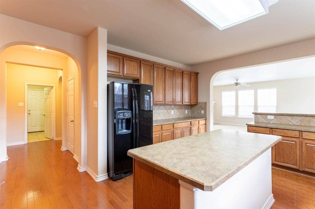 6509 Hickory Hill Drive, Plano, TX 75074 Kitchen featuring wood-finish flooring, a central island with a solid surface countertop, wood cabinetry, and a tile backsplash