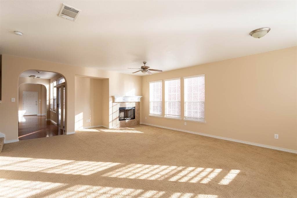 6509 Hickory Hill Drive, Plano, TX 75074 Carpeted living area featuring a fireplace with a stone surround, three windows with blinds, a ceiling fan, and an arched entry