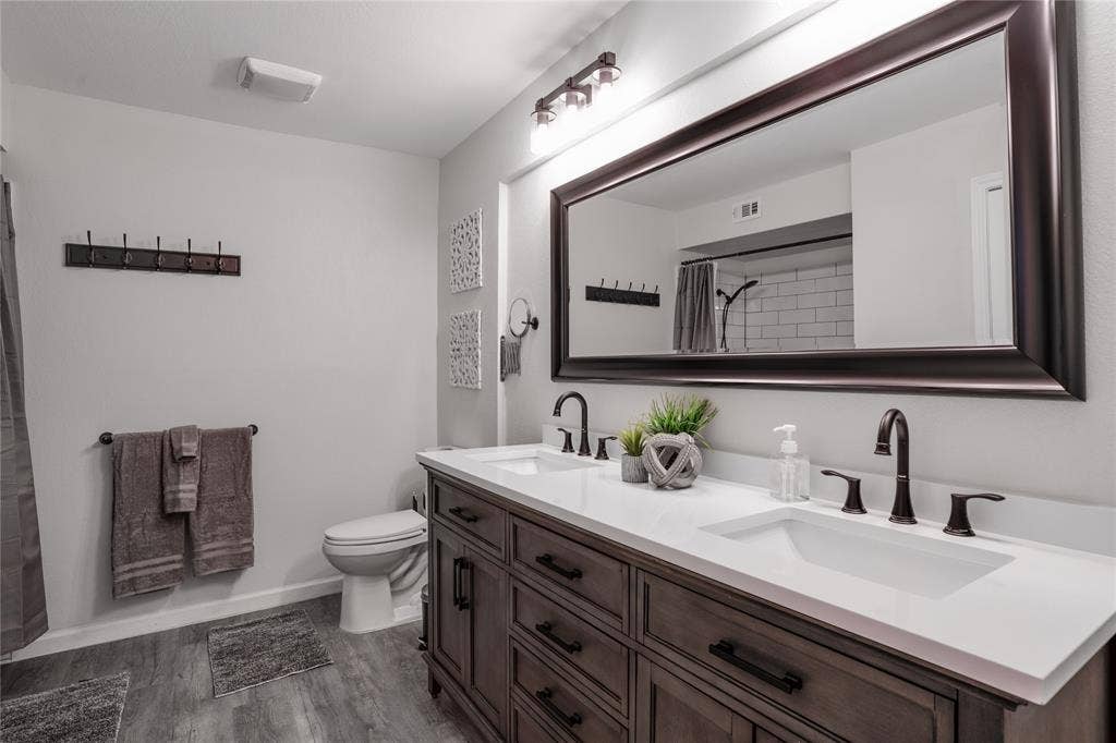 Dual sink vanity with dark wood-finish cabinetry, white countertops, and bronze-finish fixtures