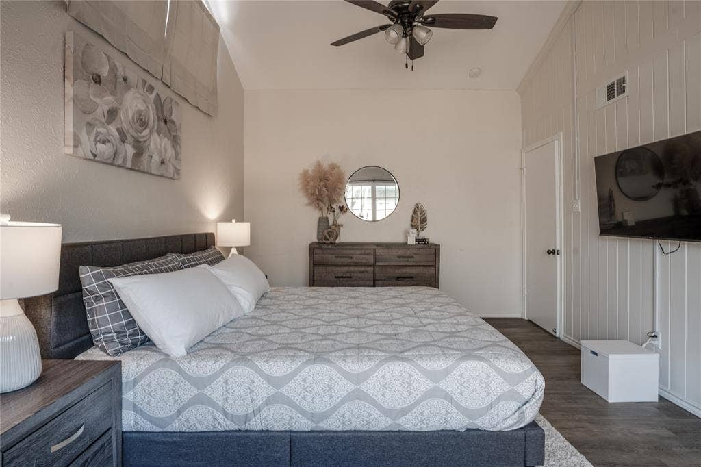 Vaulted ceiling, ceiling fan, wood-finish flooring, white panel accent wall, and built-in wall-mounted television bracket