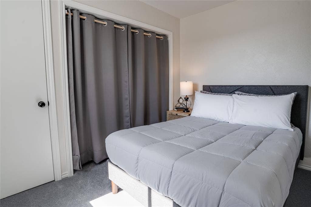 Carpeted flooring, white interior door with a black knob, and a gray fabric headboard