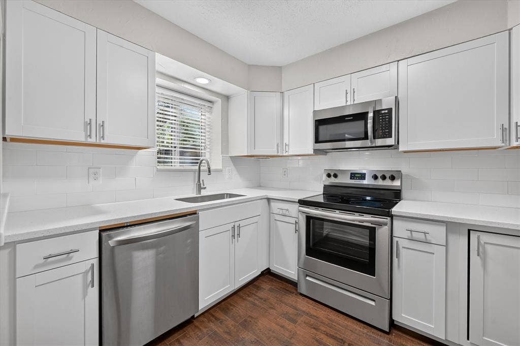 5043 Les Chateaux Drive, #214, Dallas, TX 75235 Kitchen featuring white shaker-style cabinetry, stainless steel appliances, white subway tile backsplash, and vinyl plank wood like -finish flooring
